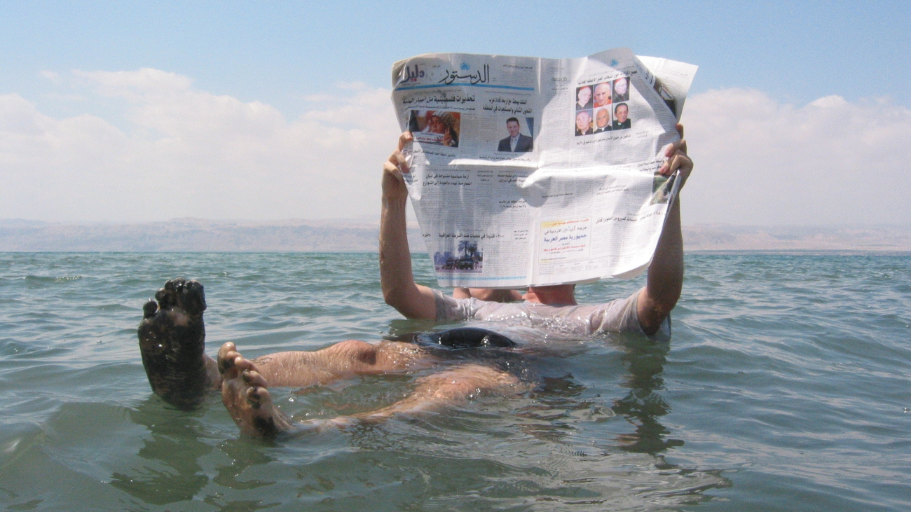 Man drijft in de Dode Zee en leest de krant. Dit is mogelijk door de grote hoeveelheid zout.