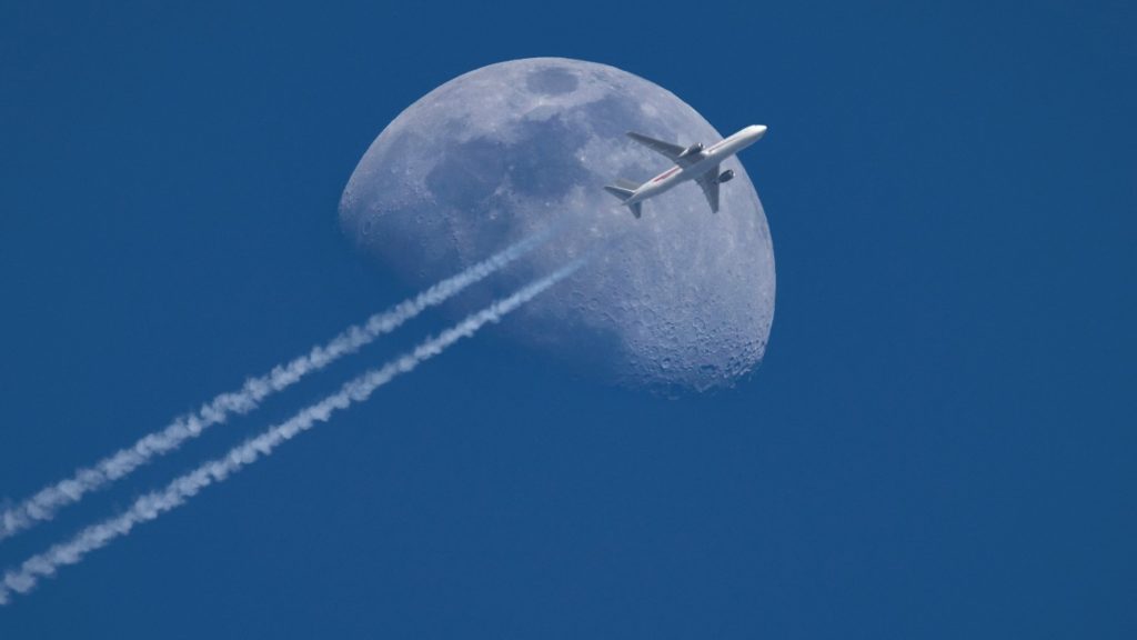 Een vliegtuig scheert voor de maan langs