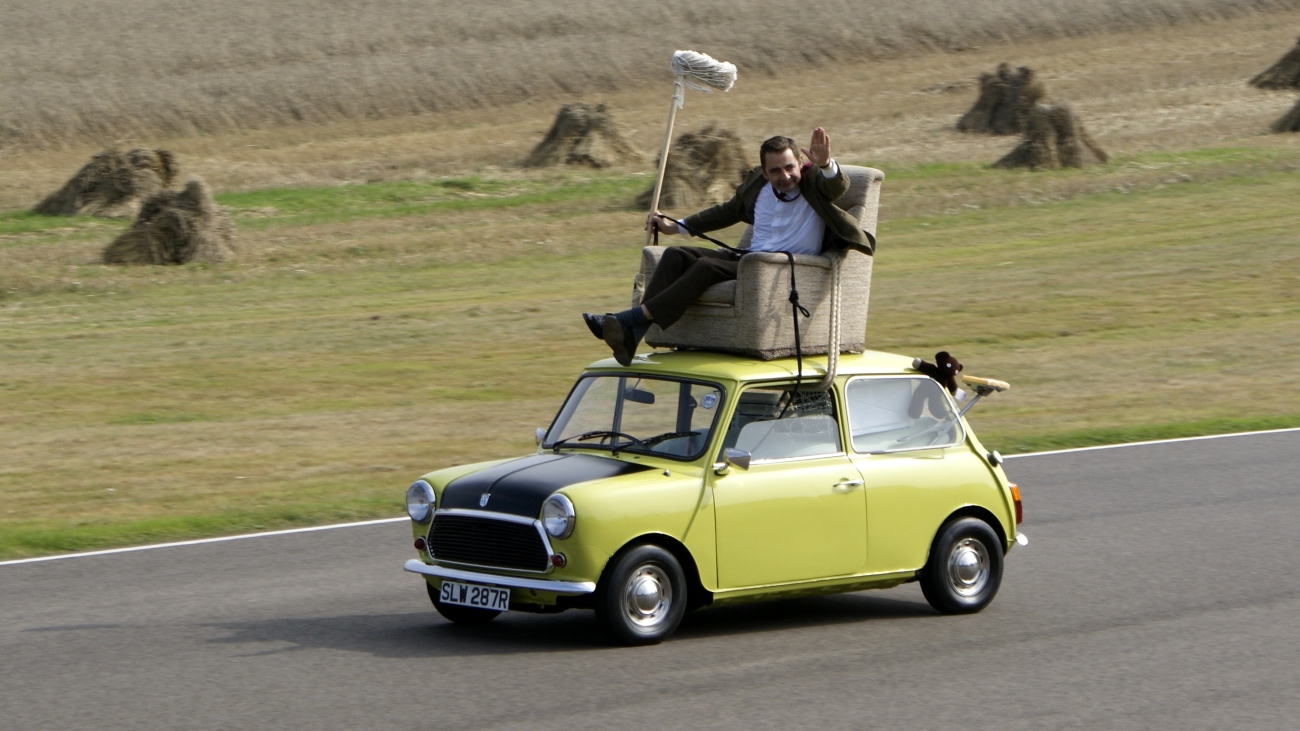 Mr. Bean op een auto. Hij denkt dat elektrische auto's niet milieuvriendelijk zijn.