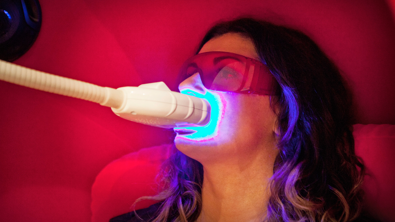 Vrouw laat haar tanden bleken en heeft een apparaat dat fel blauw licht schijnt in haar mond