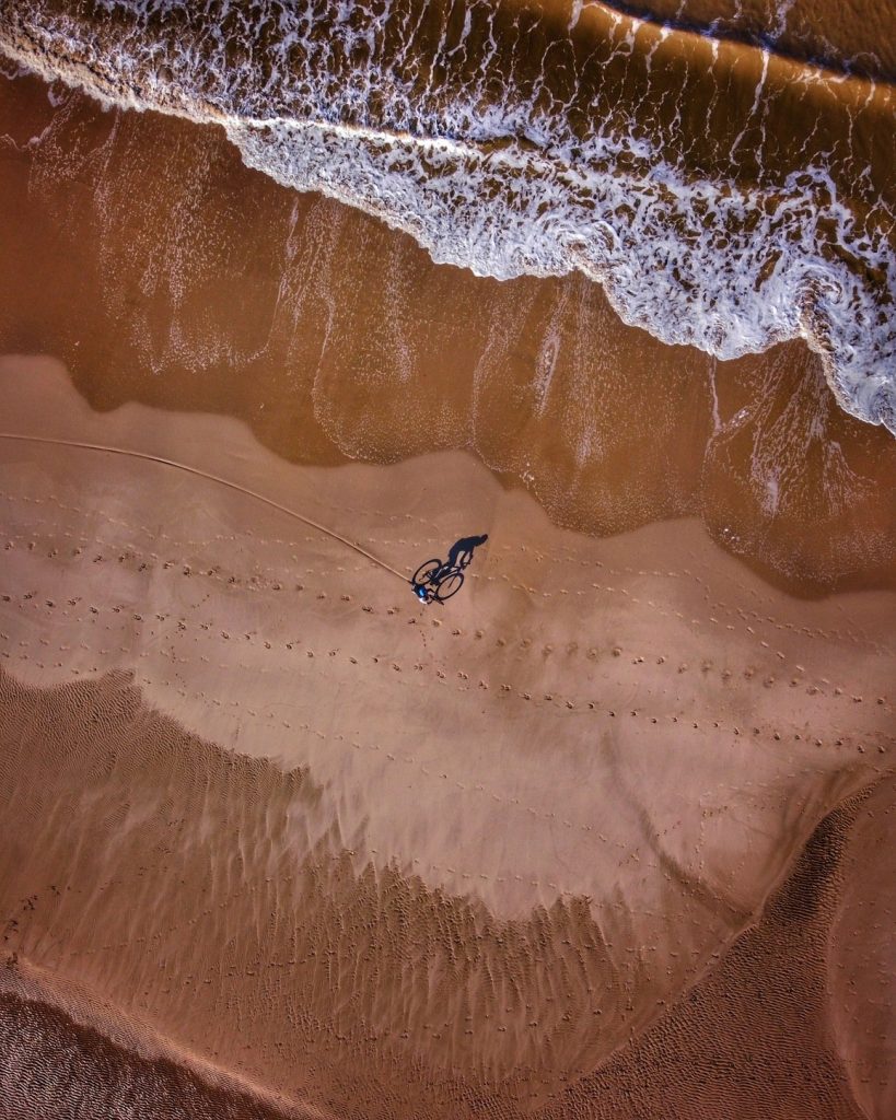 Een fietser op het strand met veel afdrukken in het zand.