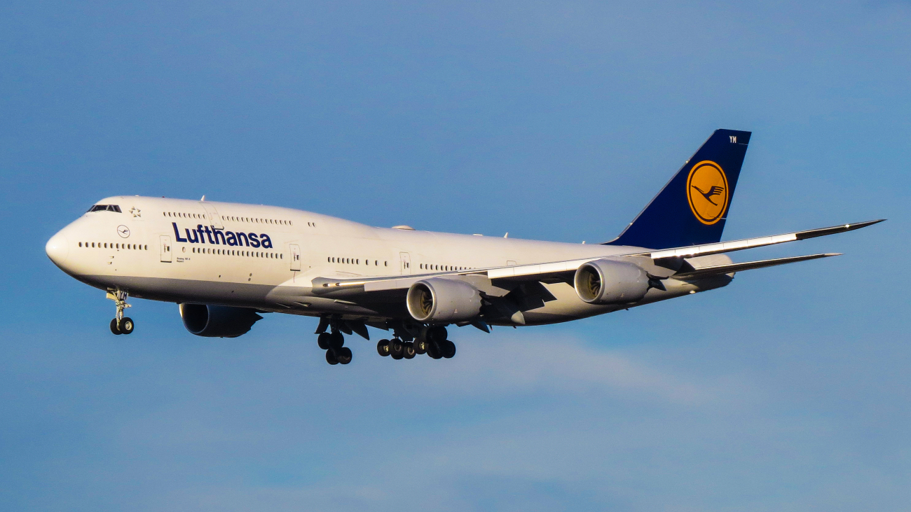 Een Boeing 747-8 van Lufthansa met vliegtuigmotoren onder de vleugels vliegt door een blauwe lucht.