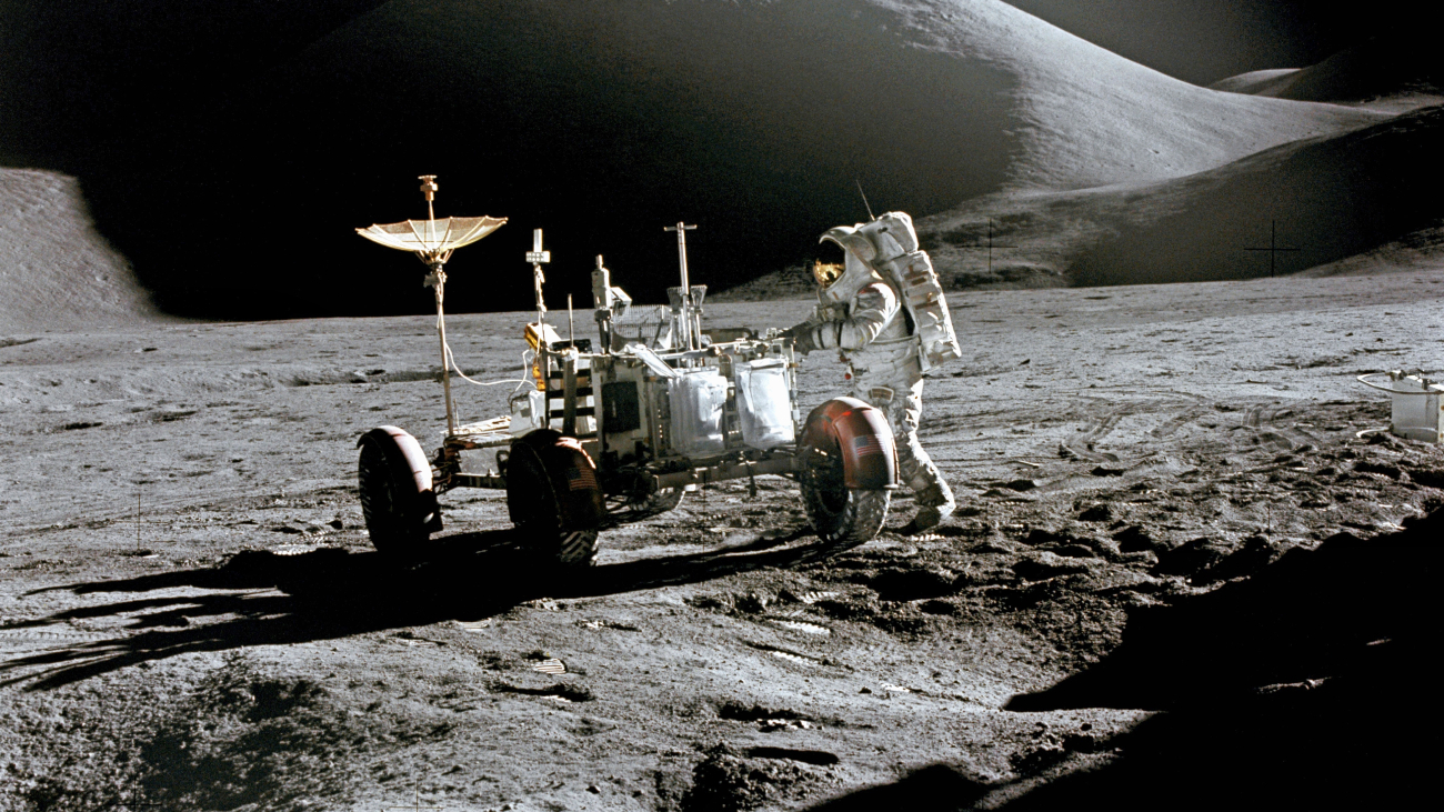 Een astronaut staat naast een auto/buggy op de maan