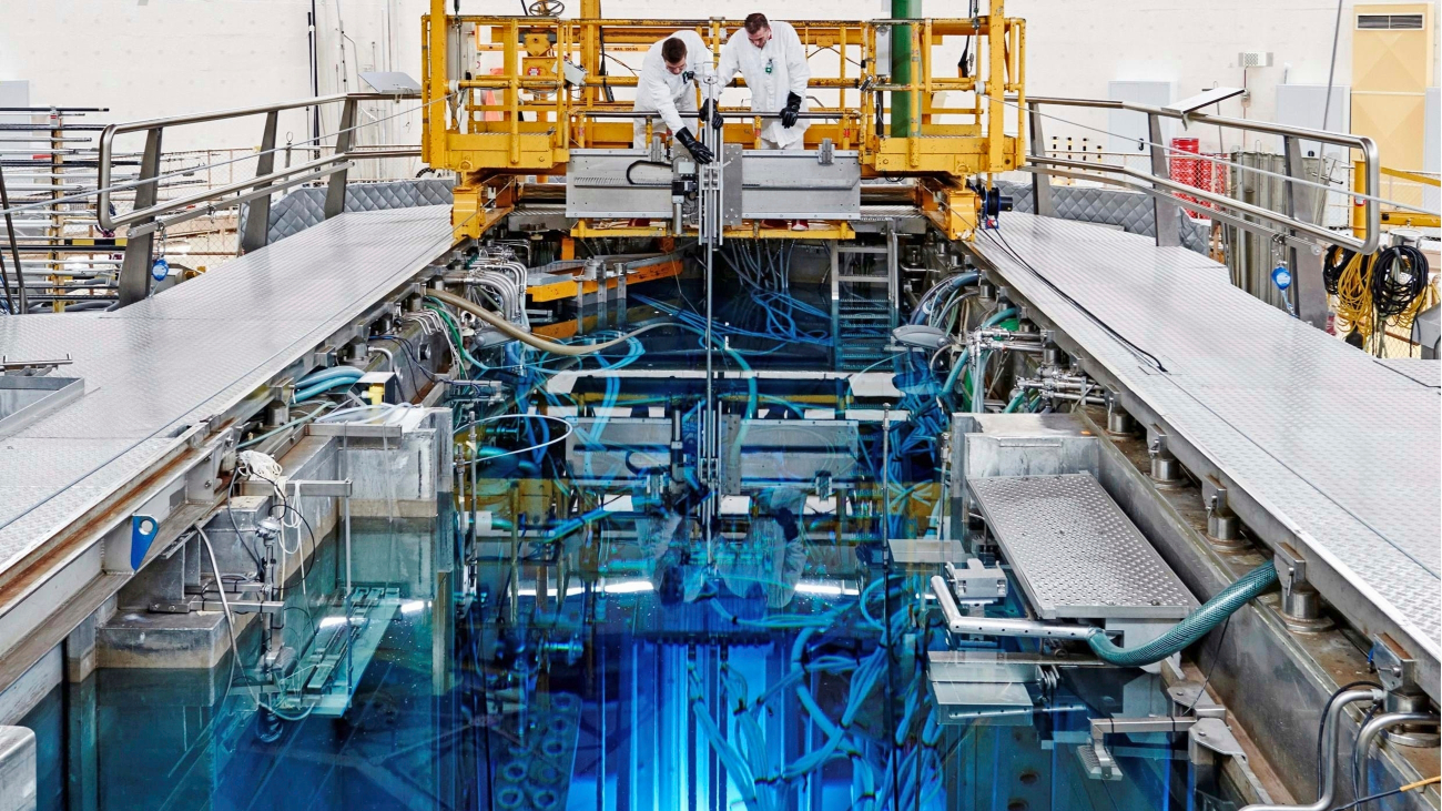 Twee personen in beschermende witte pakken doen bij een industrieel-ogende opstelling met een blauwe lichtgevende gloed onder zoek naar kernreactors op basis van gesmolten zout