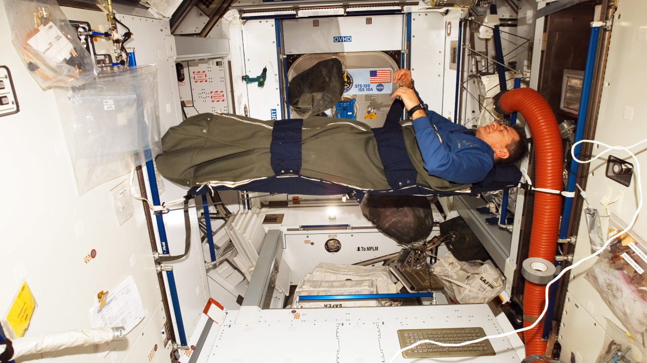 Astronaut in slaapzak vastgegespt aan de wand van het ISS klaar om te slapen