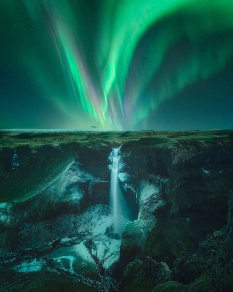 De Háifoss-waterval in IJsland met groen noorderlicht erboven