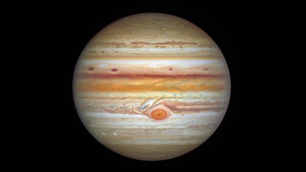 Foto van gasreus Jupiter, ziet eruit als een bol met witte, bruine en rode vlekken.