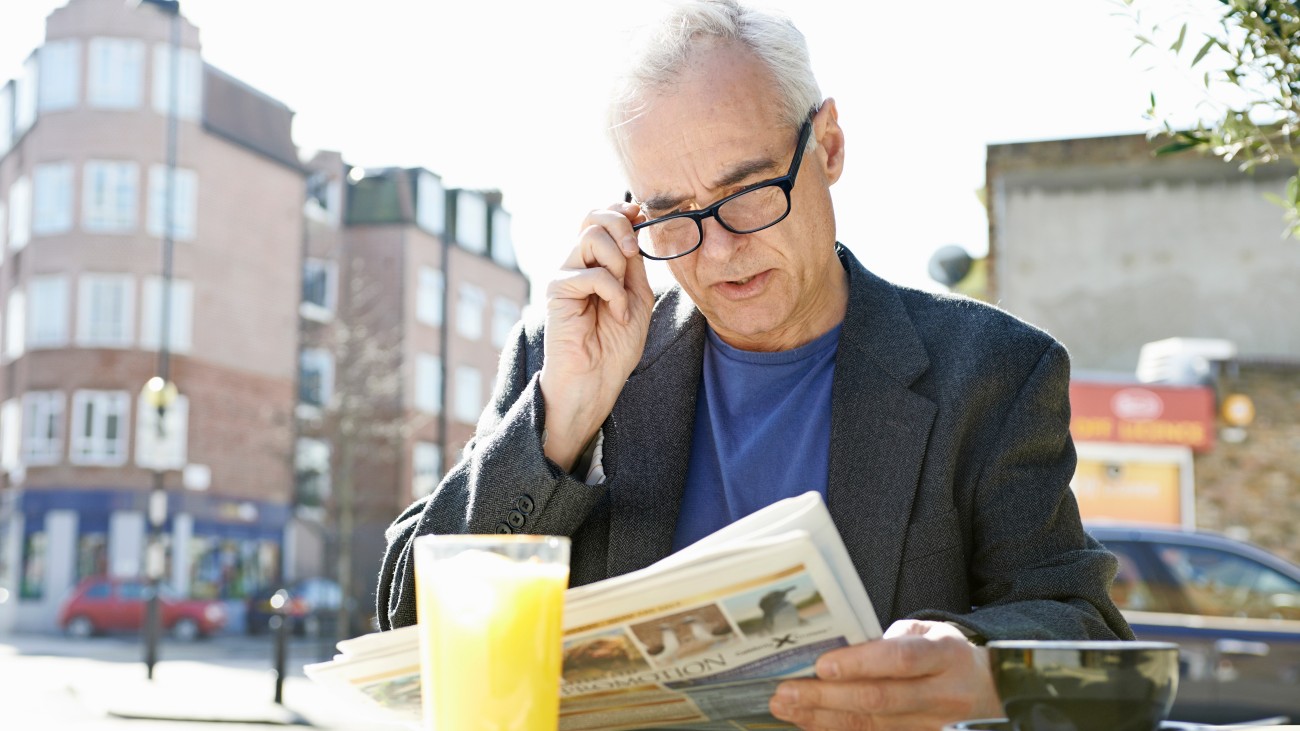 Man met leesbril leest de krant op een terras