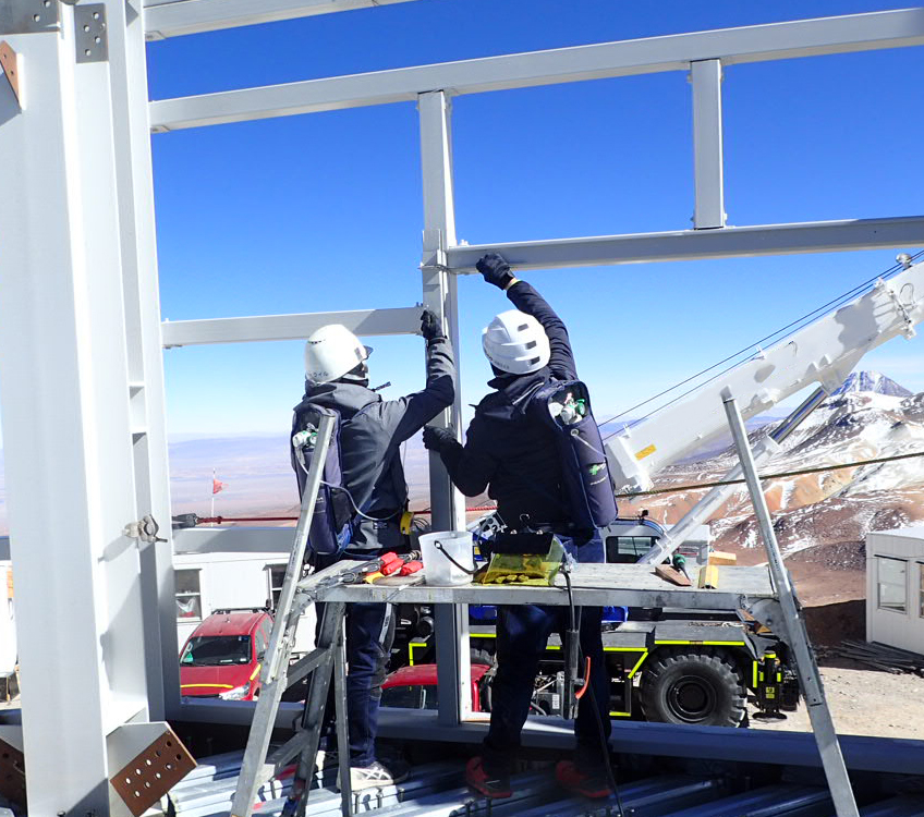 Medewerkers met zuurstofflessen op de rug tijdens de bouw van de sterrenwacht op 5640 meter hoogte