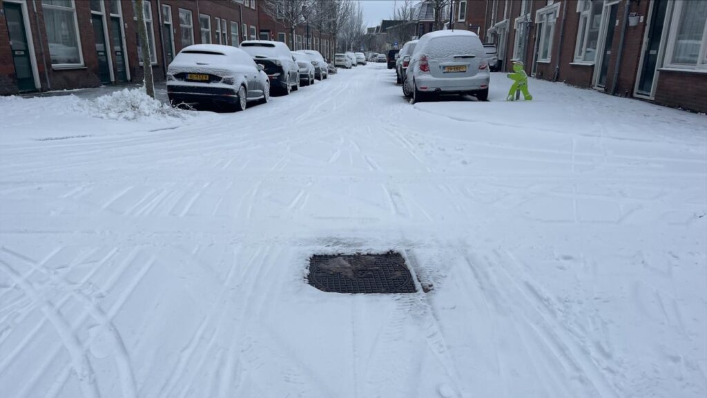 putdeksel zonder sneeuw in een besneeuwde straat