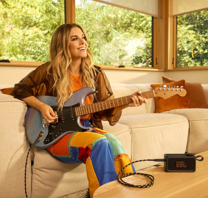 Vrouw speelt elektrische gitaar met JBL bandbox als versterker en speaker