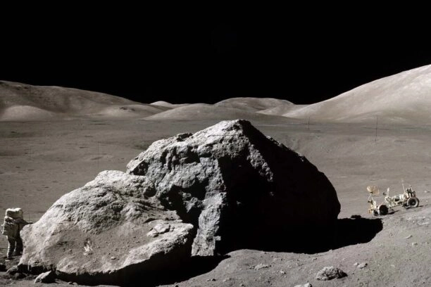 Apollo-astronaut Harrison H. Schmitt naast een grote rots op de maan en de Lunar Roving Vehicle rechts.