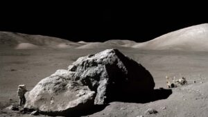 Apollo-astronaut Harrison H. Schmitt naast een grote rots op de maan en de Lunar Roving Vehicle rechts.