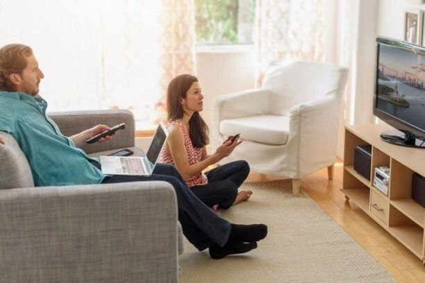 Man en vrouw kijken een film op tv, maar ze hebben allebei een tweede scherm dat hun aandacht vraagt