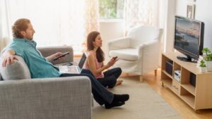 Man en vrouw kijken een film op tv, maar ze hebben allebei een tweede scherm dat hun aandacht vraagt