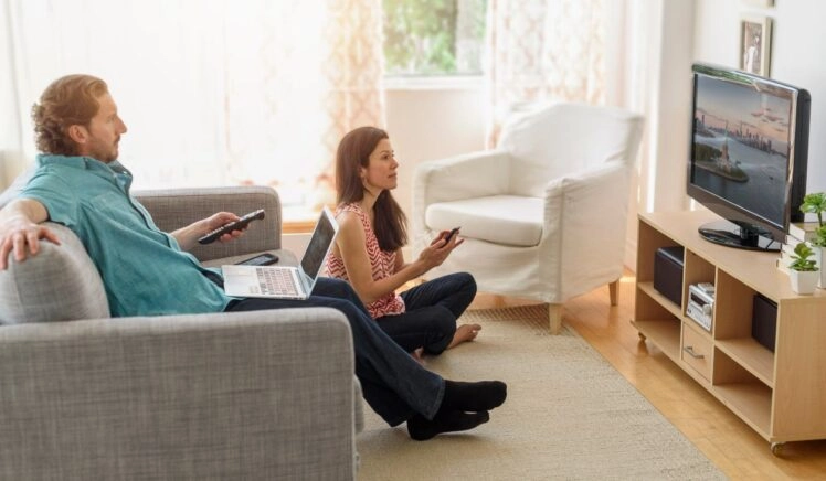 Man en vrouw kijken een film op tv, maar ze hebben allebei een tweede scherm dat hun aandacht vraagt