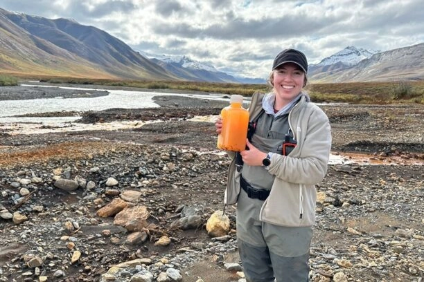 Een van de onderzoekers met een fles met oranje water uit de Igning River.