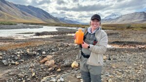 Een van de onderzoekers met een fles met oranje water uit de Igning River.